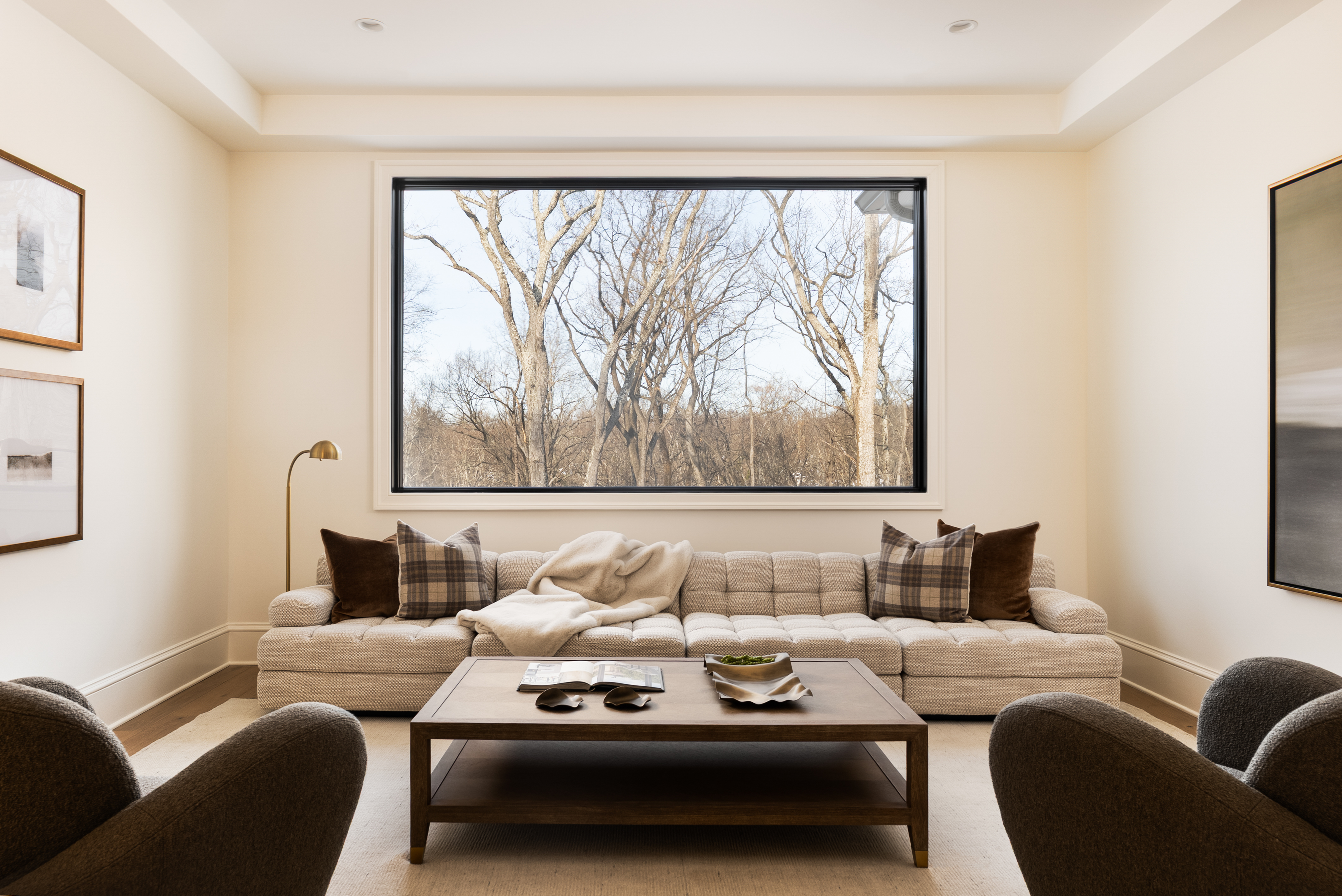 Cozy family room with deep sofa, plaid pillows, and picture window framing mature trees